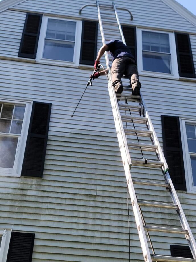Sunbright Cleaning crew member power washing home siding from a ladder