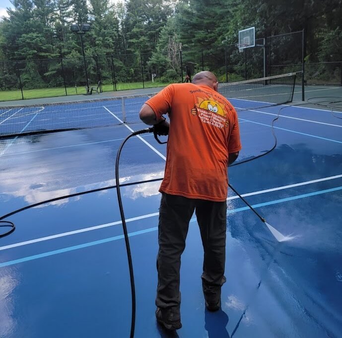 Sunbright Cleaning crew member power washing a backyard sport court